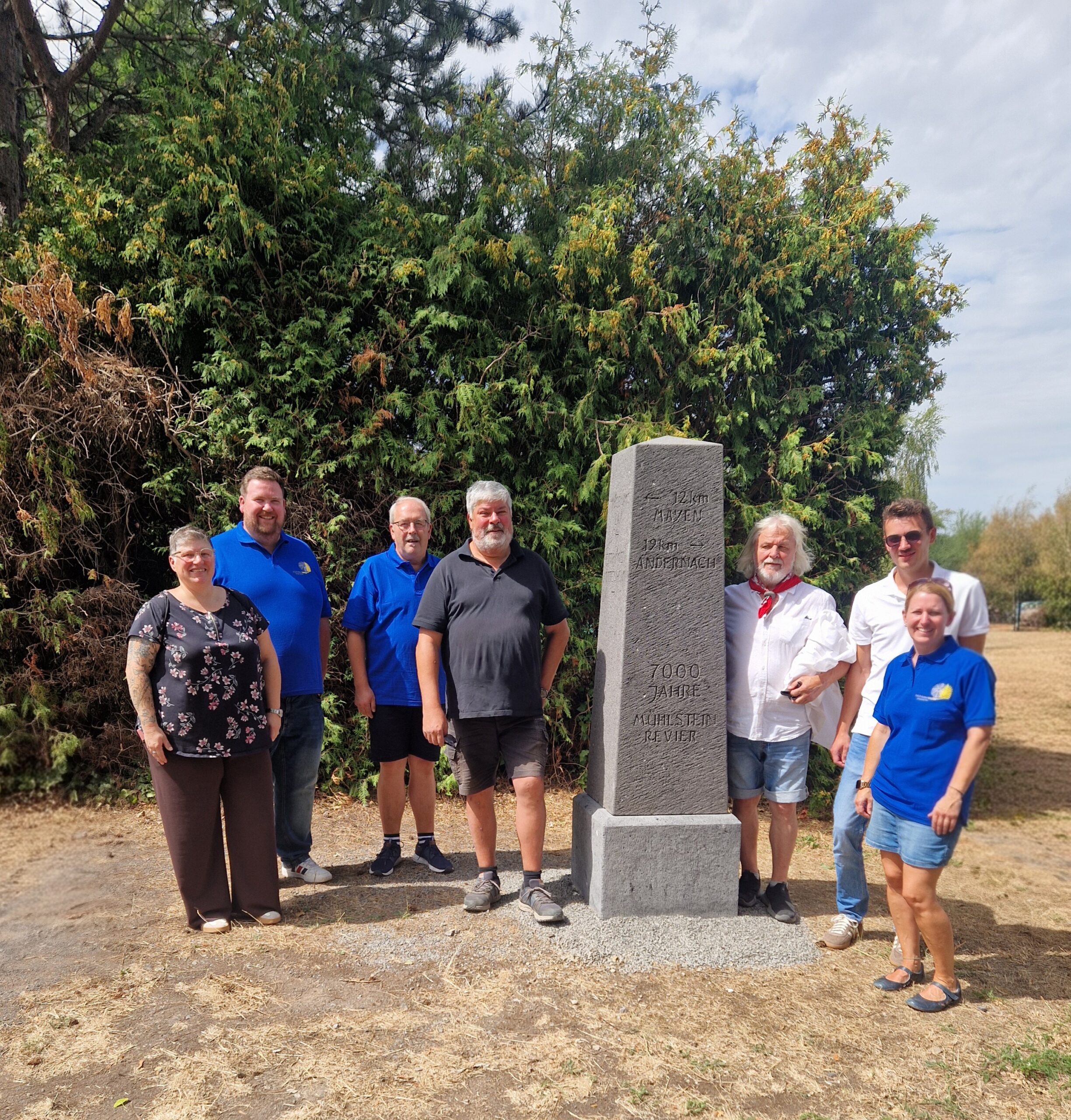 Sieben Personen stehen um einen Meilenstein, der auf das Gebiet des Mühlsteinreviers RheinEifel hinweist.
